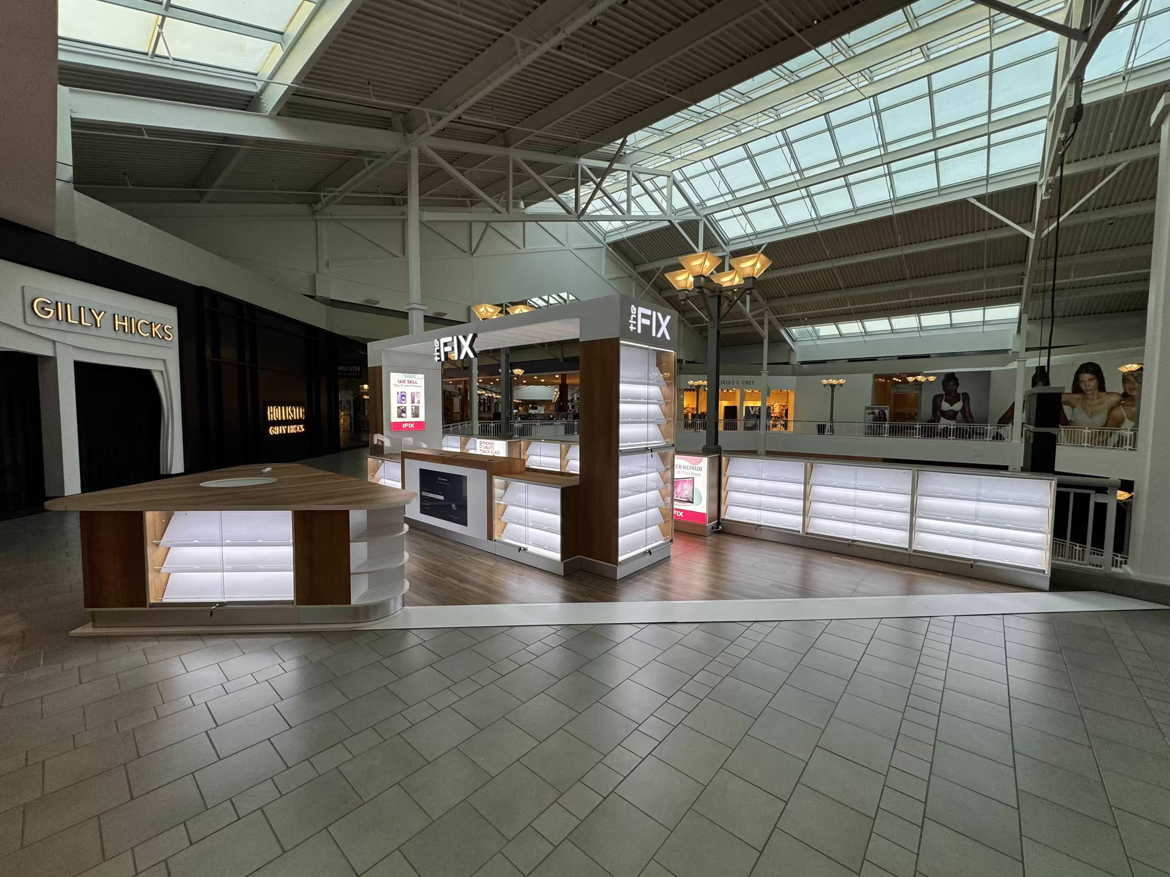 Quiosco de The Fix en Bridgewater Commons — vitrinas iluminadas bajo un atrio con tragaluz