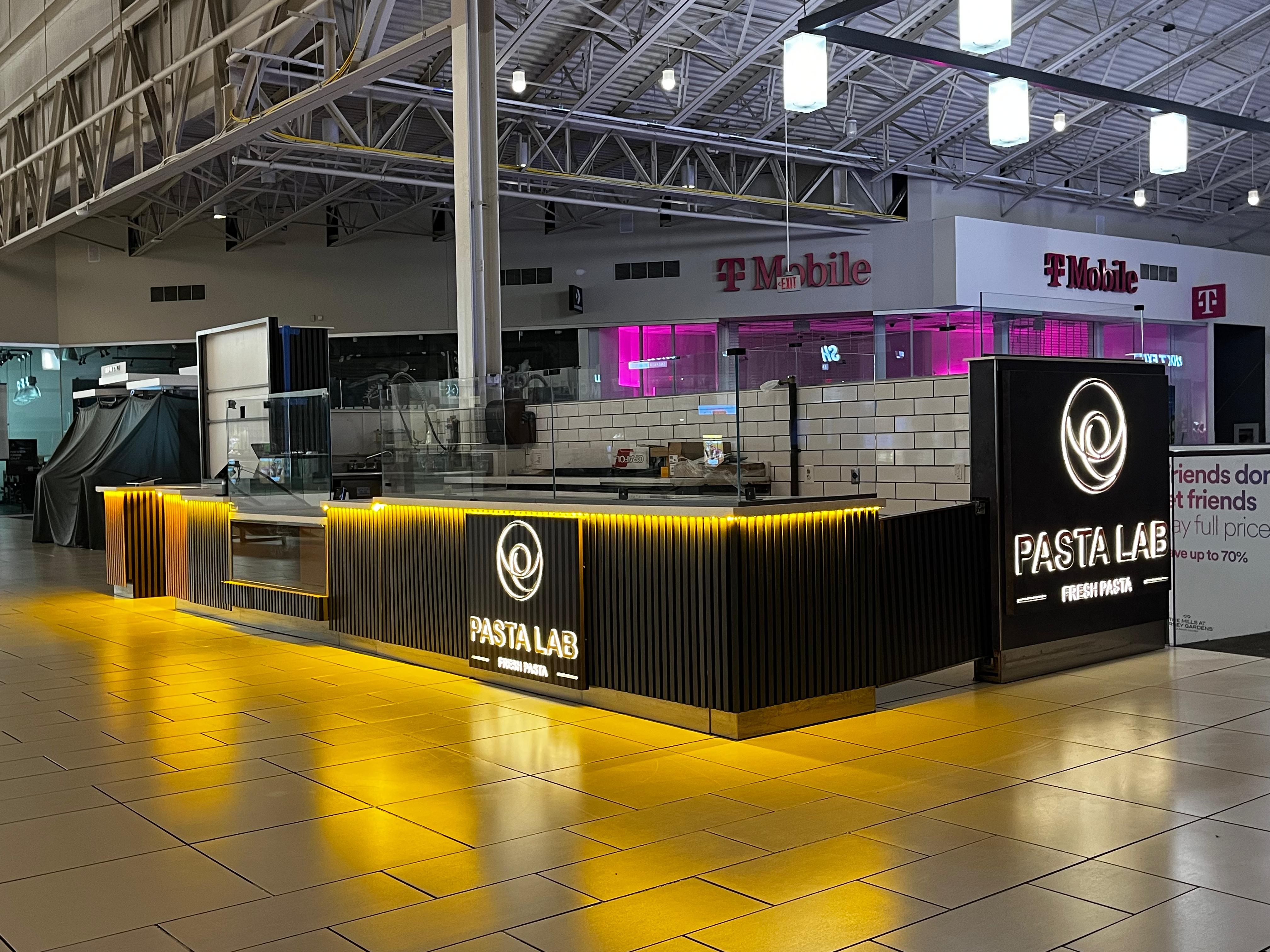 Quiosco de Pasta Lab — ebanistería negra con acentos dorados y panel de marca iluminado