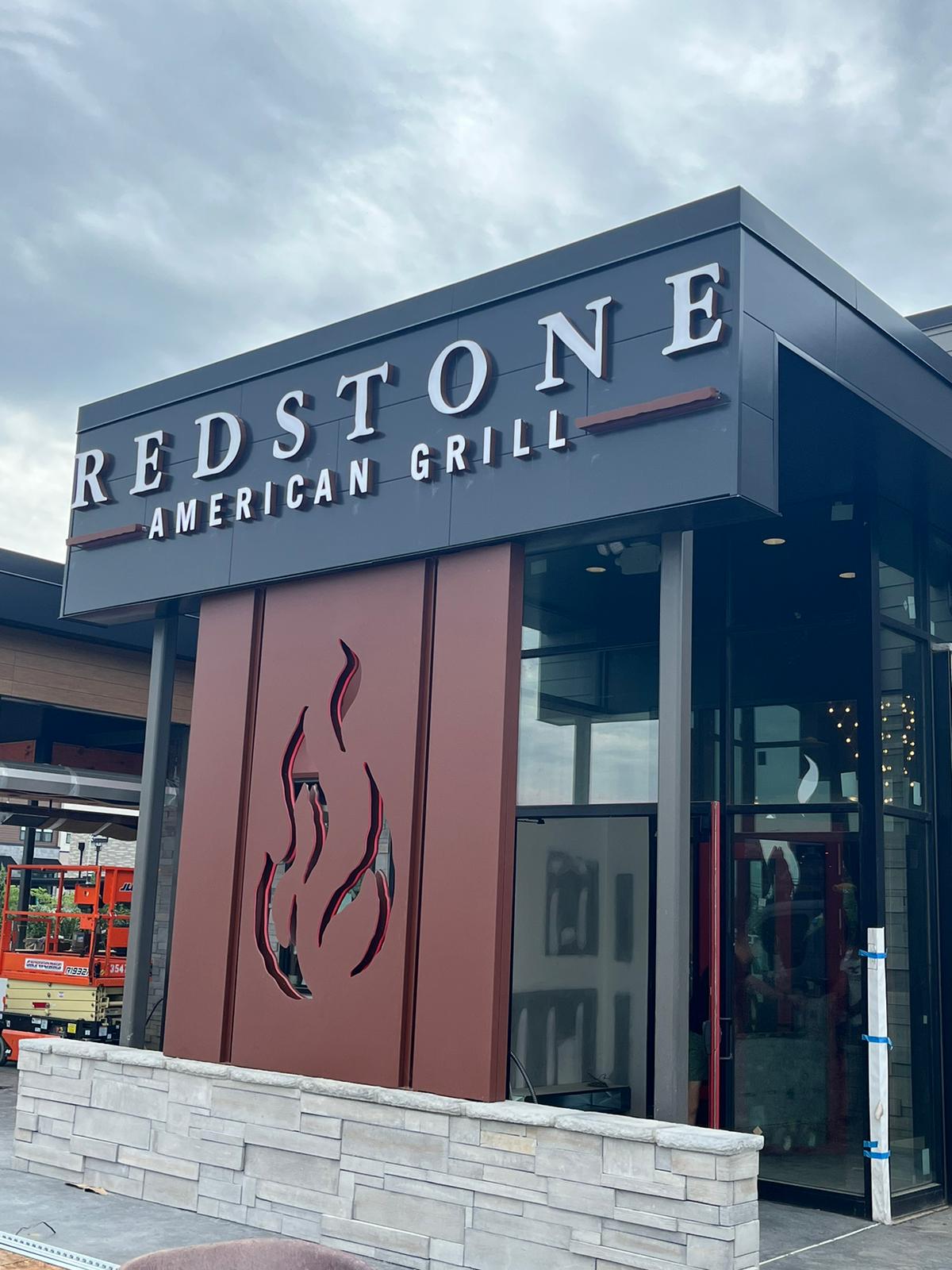 Letrero iluminado de letras corpóreas y logotipo dimensional de llama en la entrada de Redstone American Grill
